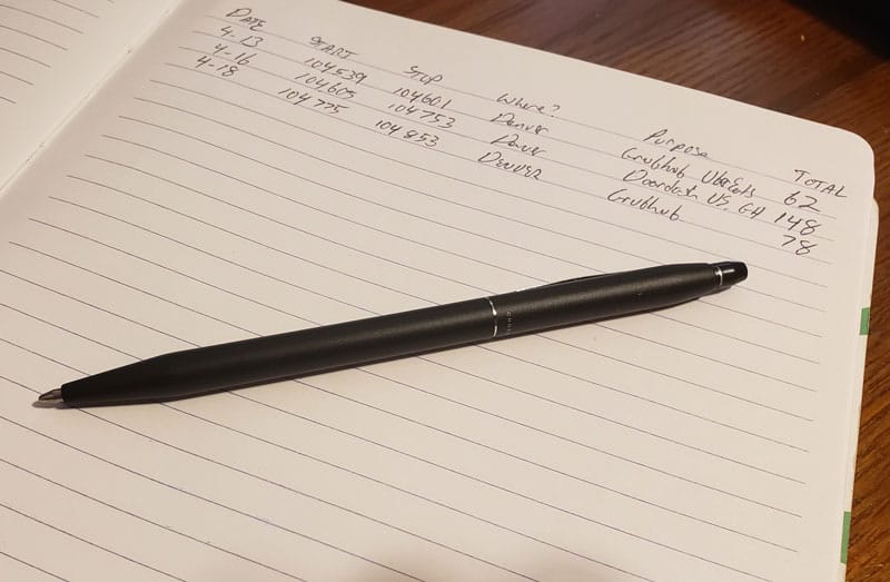 A pen on top of a mileage log that includes handwritten records of the date of trips, odometer readings for the start and end of a trip, where the trip went, business purpose and total miles.