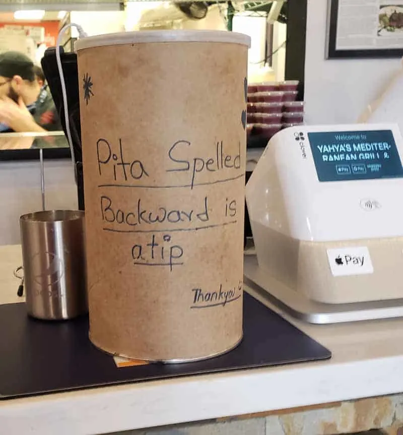 A tip jar at a Mediterranean restaurant with a handwritten sign that says Pita spelled backwards is a tip.