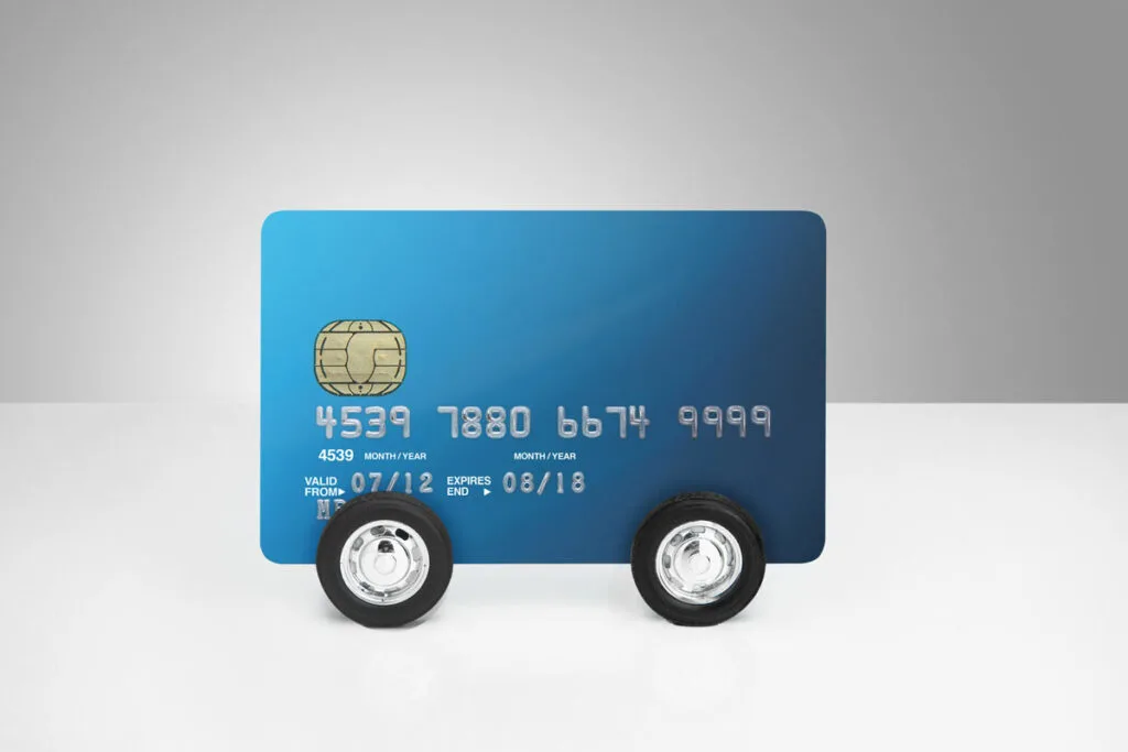 Illustration of a credit card that has wheels on it, illustrating how future costs pile up with each mile driven.