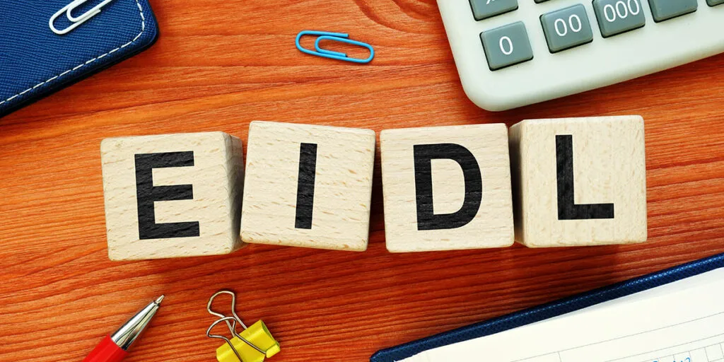 blocks with letters E. I. D. L. sitting on a desktop with a pen, paper clips, calculator and notebooks.