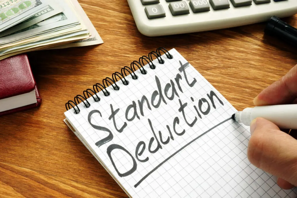 An independent contractor deciding between standard or itemized deductions misspells it as Standart, writing on a table next to calculator and stack of money.