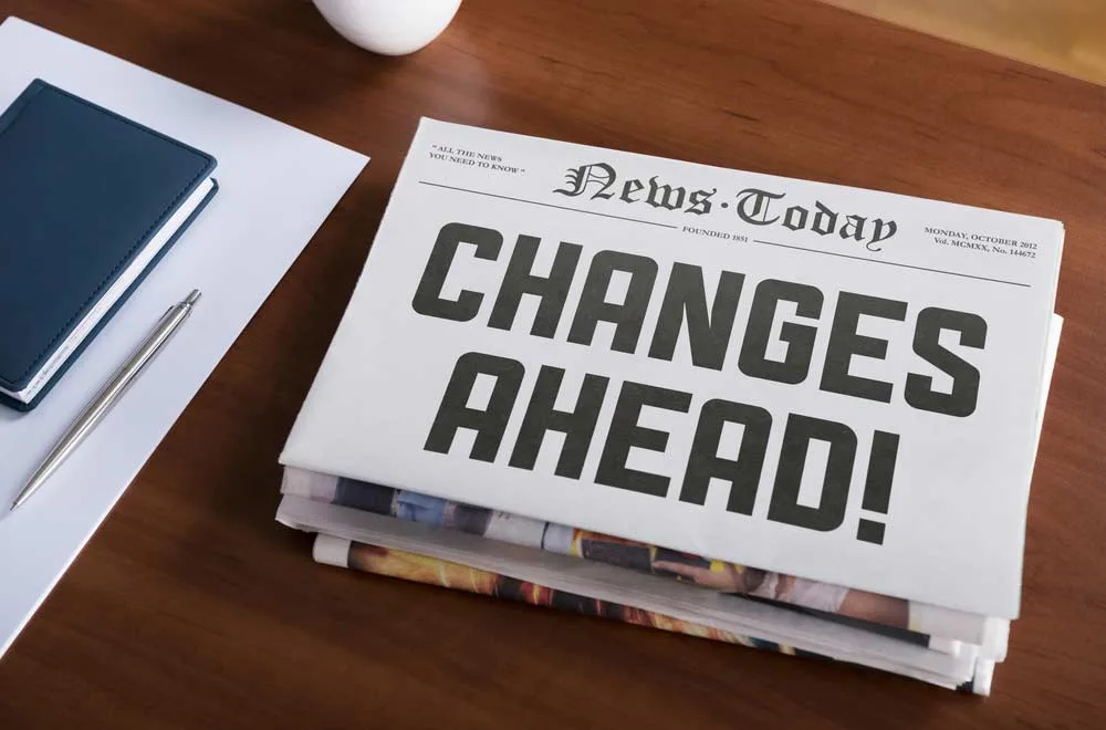 Business desktop with paper, notebook, pen, and a stack of business newspapers with the headline on the top paper saying Changes Ahead!