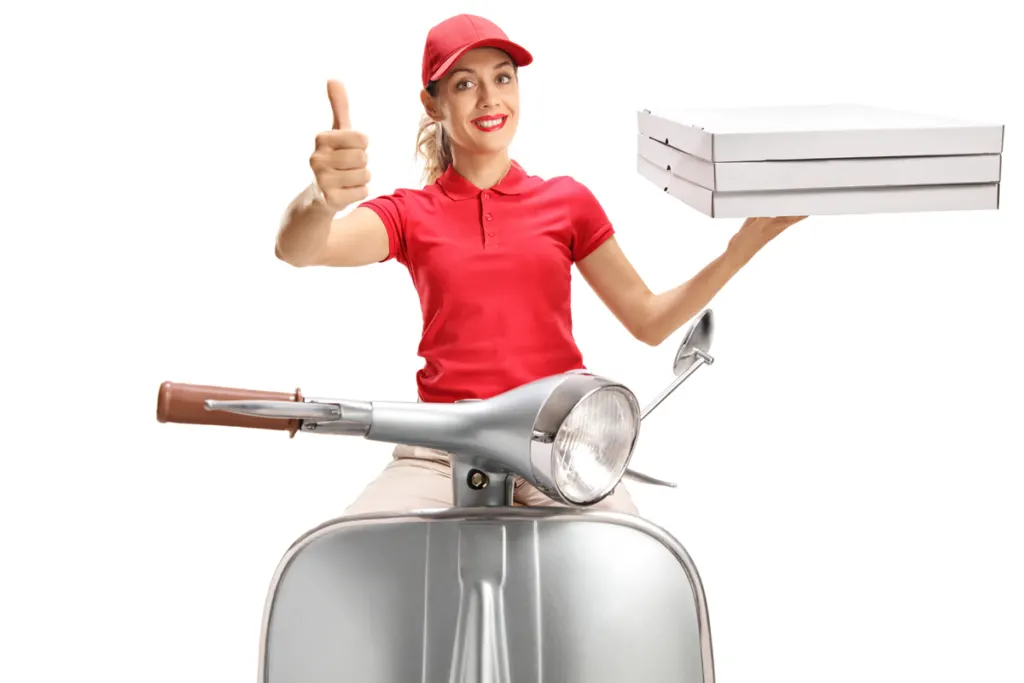 A female Uber Eats driver in a red shirt and cap sitting on a scooter, holding three pizzas and holding her thumb up in the air with a smile.